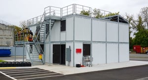 Multi-level modular fire training tower with exterior stairs and firefighters preparing for training exercises.